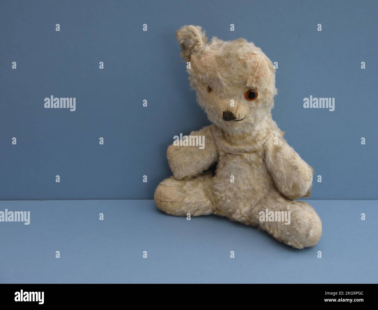 Klassischer Teddybär in liebenswertem, getragenem Zustand mit fehlendem Auge, fehlendem Ohr und fehlendem Fell. Mit blauem Hintergrund und Platz links für die Beschriftung. Stockfoto