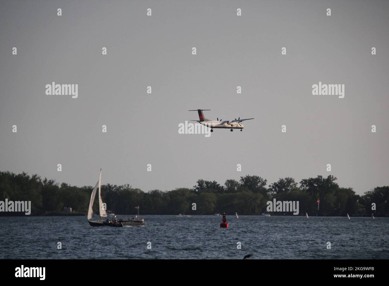 Ein weißes Flugzeug überquert ein Segelboot mit Bäumen im Hintergrund Stockfoto