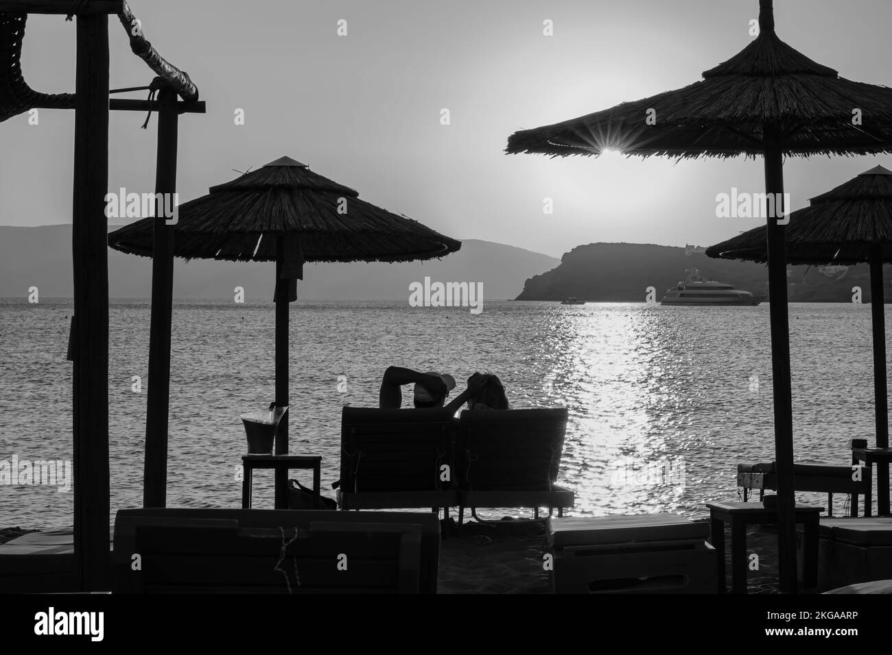IOS, Griechenland - 13. September 2022 : Blick auf ein Paar, das auf Sonnenliegen liegt, Wein trinkt und den herrlichen Sonnenuntergang in Orange in iOS Greece genießt Stockfoto
