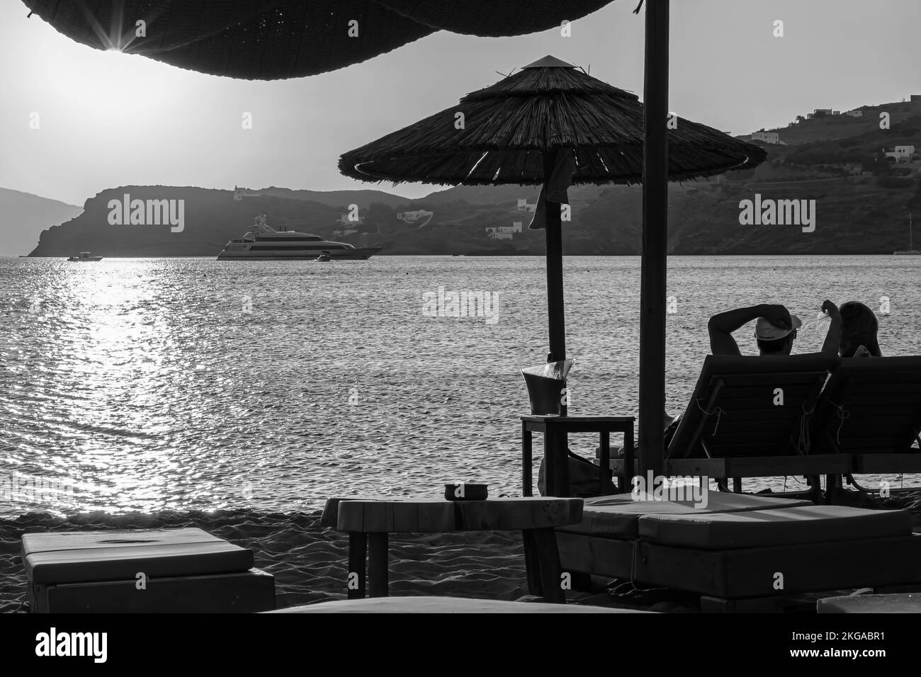 IOS, Griechenland - 13. September 2022 : Blick auf ein Paar, das auf Sonnenliegen liegt, Wein trinkt und den herrlichen Sonnenuntergang in Orange in iOS Greece genießt Stockfoto