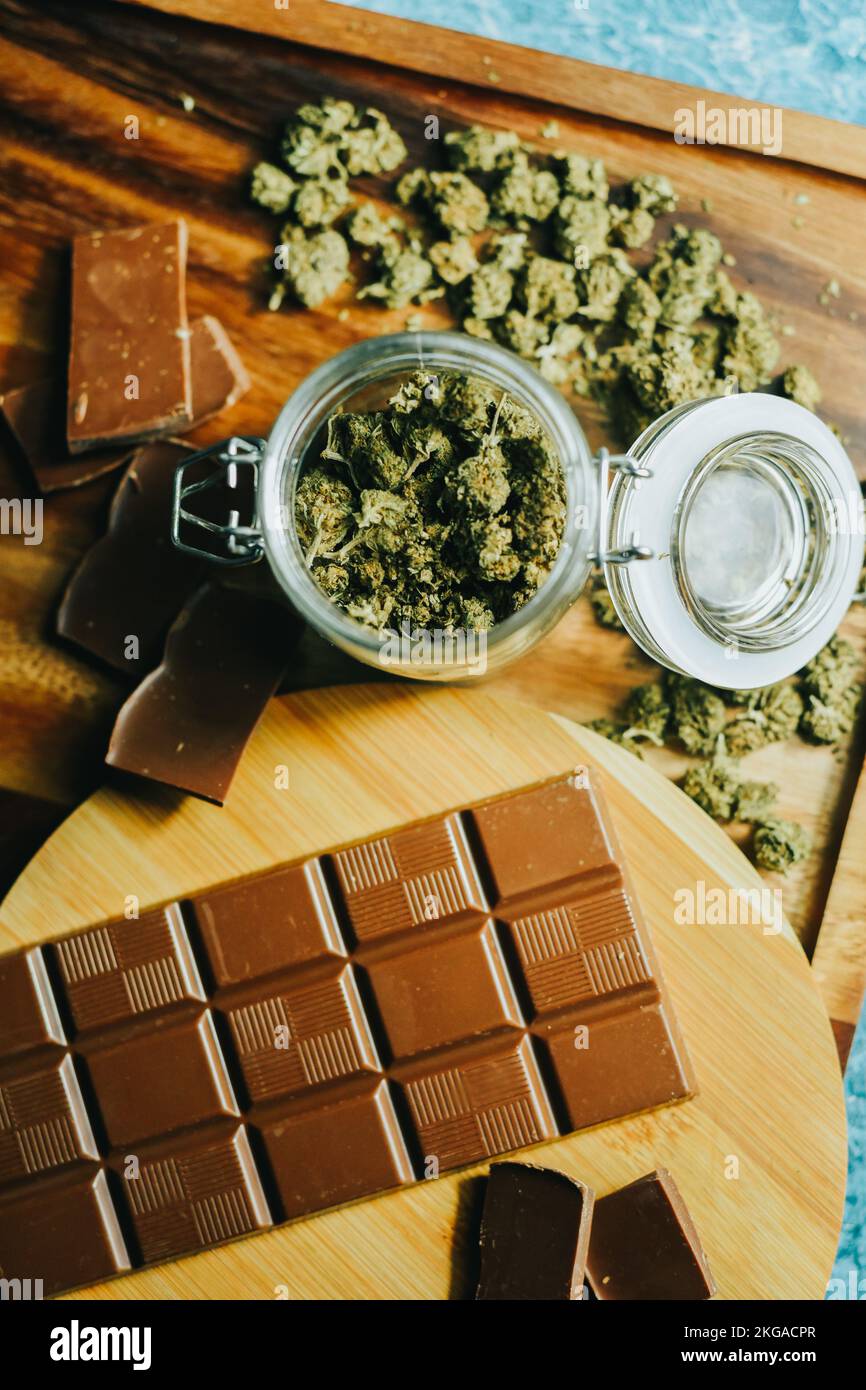 Schokolade mit Marihuana auf dem Hintergrund eines Holztischs und Marihuana-Zapfen. CBD und THC, Sativa und Indica. Marihuana-Gras im Futter Stockfoto