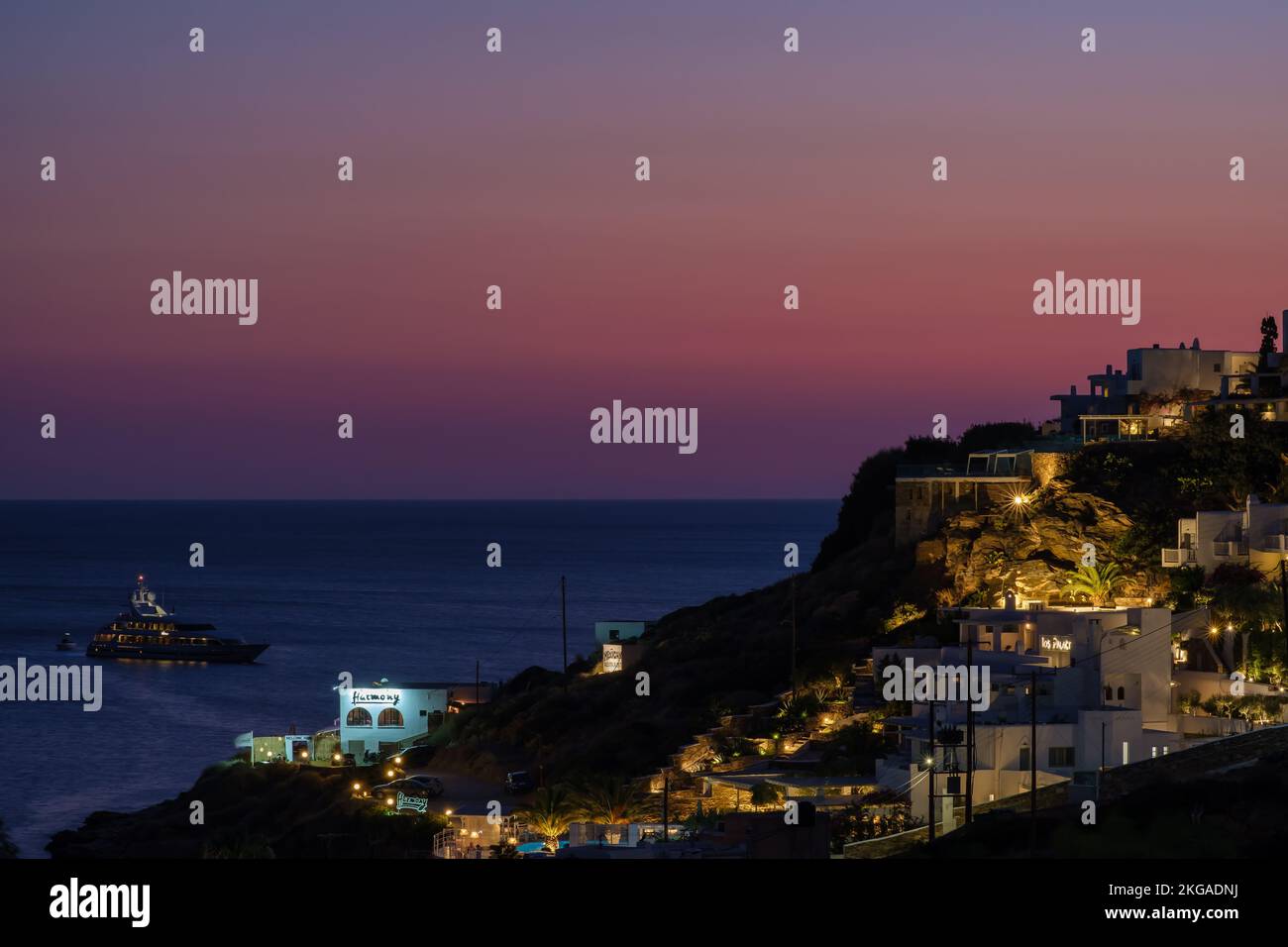 IOS, Griechenland - 13 . September 2022 : Blick auf einen atemberaubenden violetten Sonnenuntergang, eine Yacht und die beleuchteten, malerischen Hotels und Restaurants in iOS Greece Stockfoto