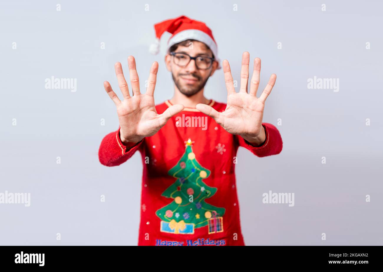 Ein Mann mit weihnachtsmütze zählt Nummer zehn mit den Fingern. Weihnachtlicher junger Mann, der Nummer zehn mit Händen zählt. Der Begriff des Menschen in der weihnachtskostümbilanz Stockfoto