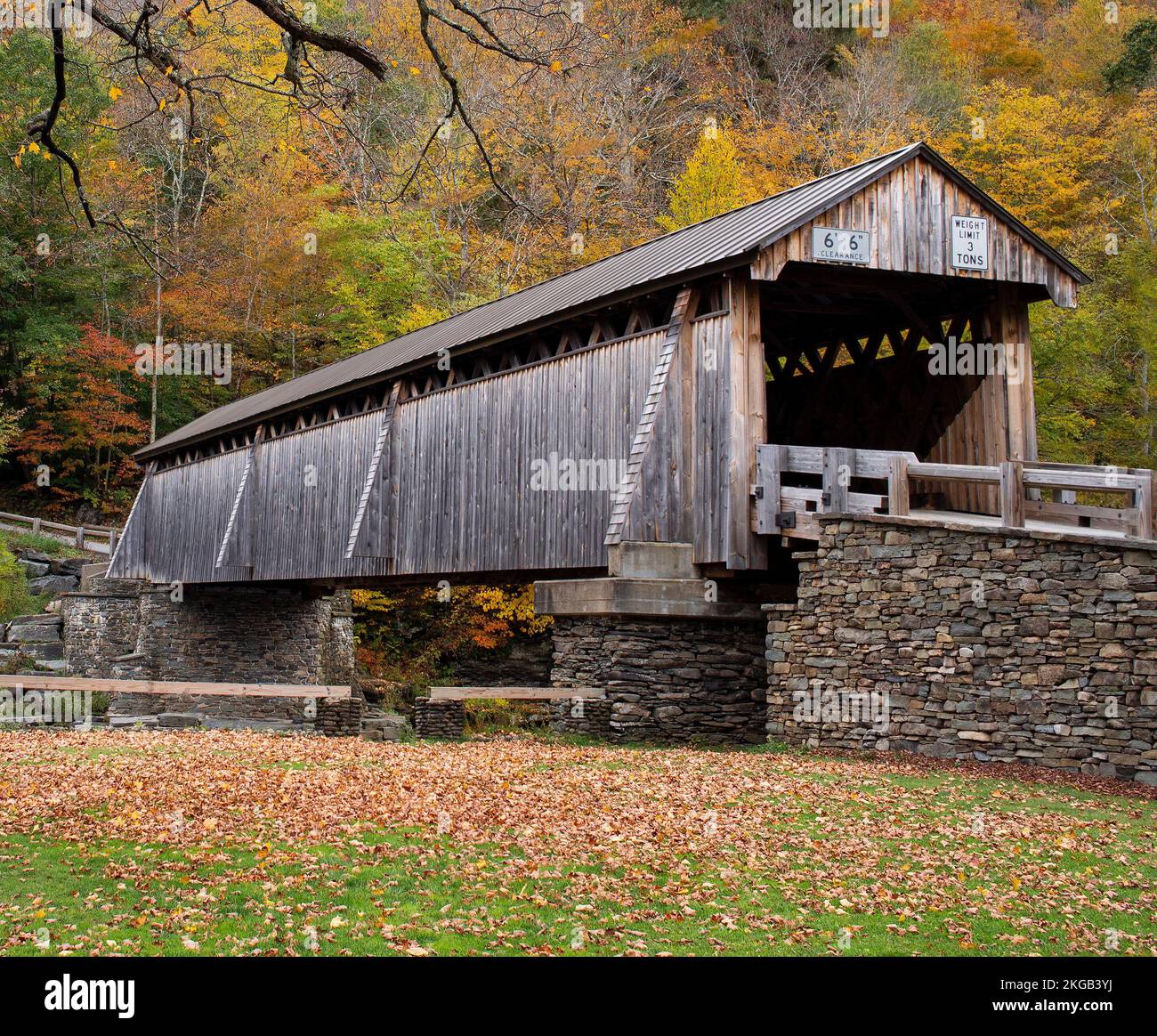 Ländliche, hölzerne überdachte Brücke über einen ruhigen Fluss, lebhafte Herbstblattfarben in den bewaldeten Hügeln. Der Herbsttag ist frisch. Stockfoto