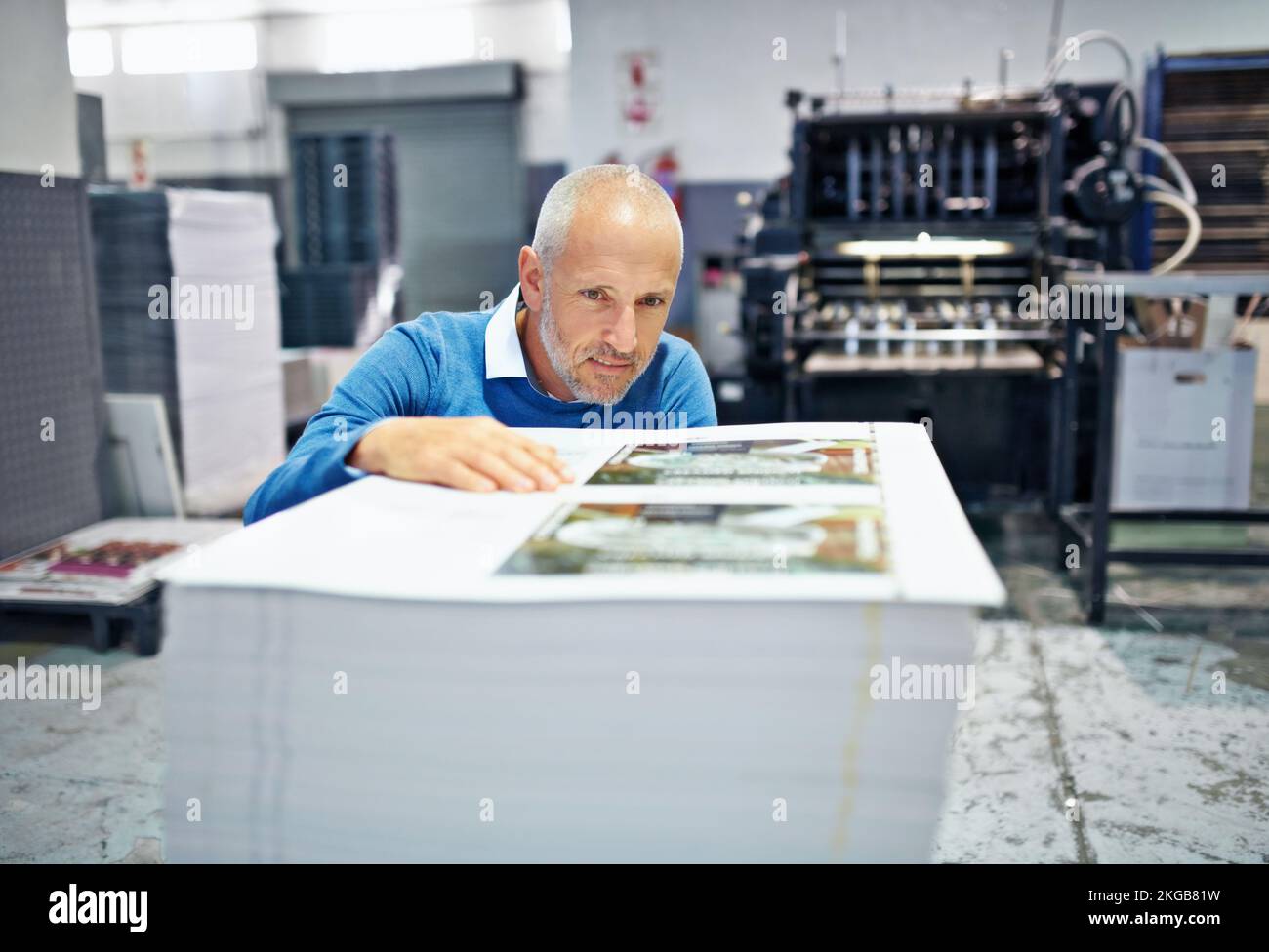 Einen anderen Blickwinkel auf das Problem zu gewinnen. Ein Mann, der die Qualität eines Druckdurchlaufs in einer Fabrik prüft. Stockfoto
