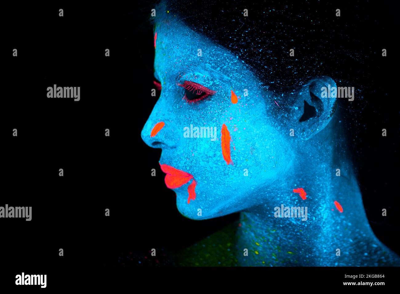 Schönheit unter schwarzem Licht. Eine junge Frau, die mit Neonfarbe im Gesicht posiert. Stockfoto