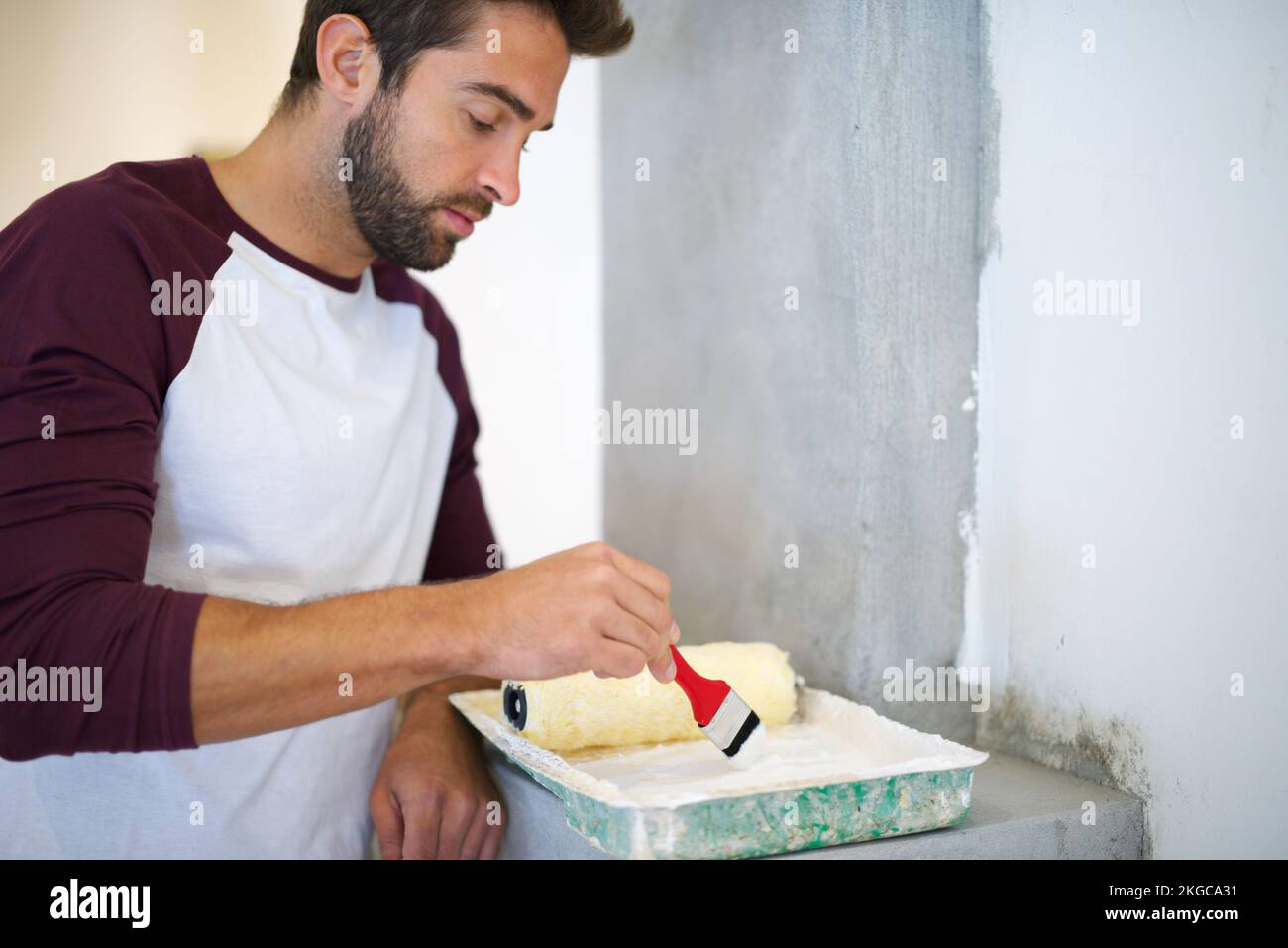 Heimwerkerbedarf. Ein junger Mann, der drinnen eine Wand malt. Stockfoto