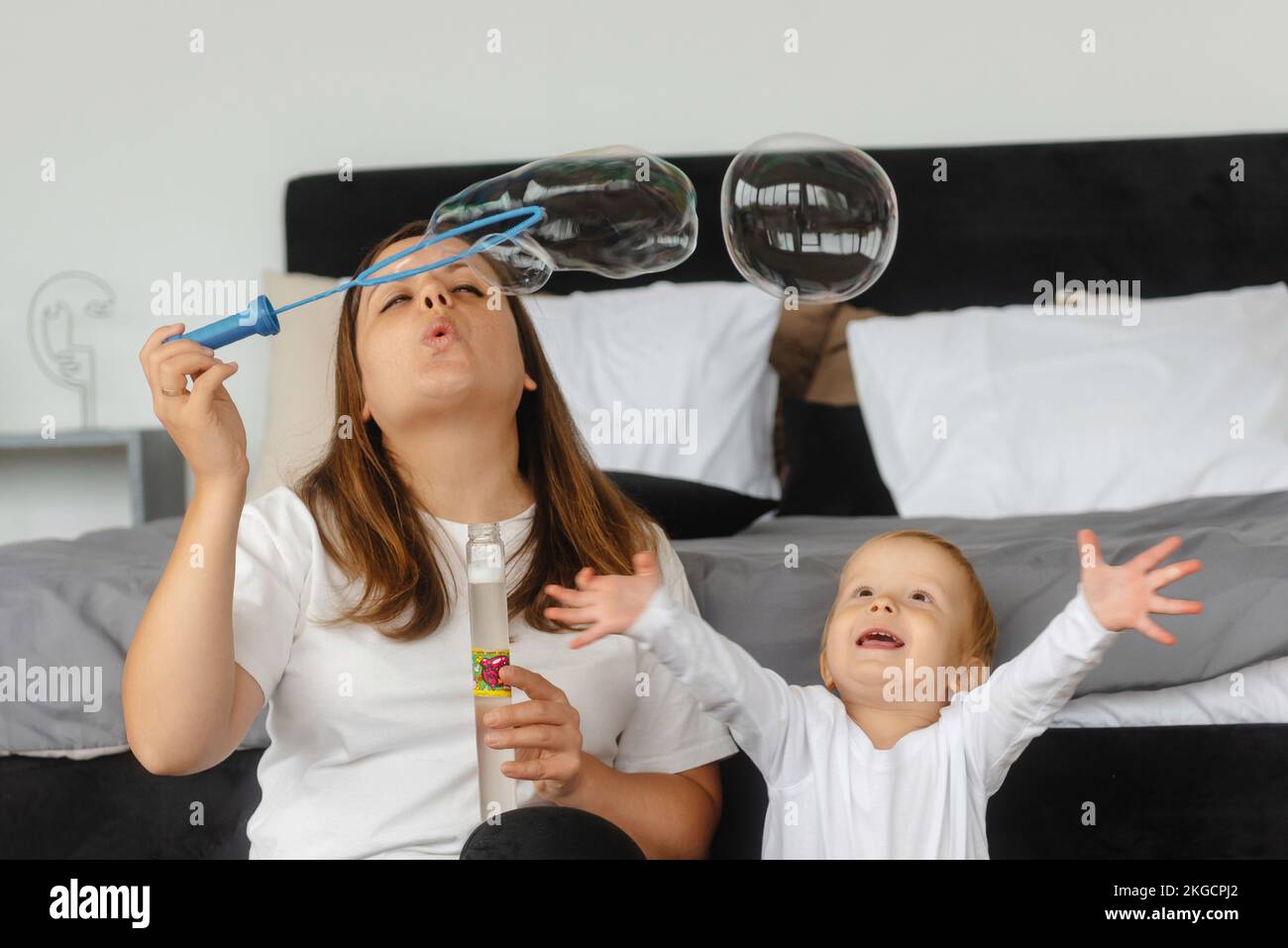 Mutter und Sohn spielen mit Seifenblasen. Das Kind genießt die Seifenblasen. Die Familie sitzt zu Hause und spielt mit Seifenblasen Stockfoto