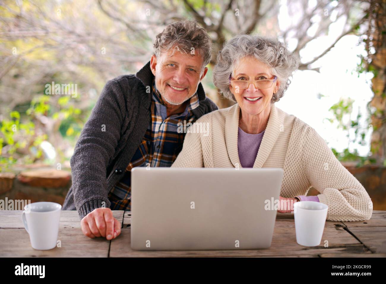Kaffee und ein gemütlicher Spaziergang. Porträt eines älteren Ehepaars, das draußen mit einem Laptop sitzt. Stockfoto