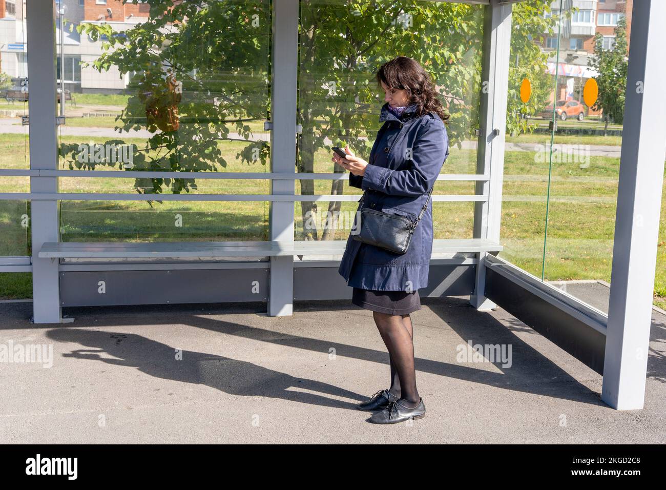 Frau liest Informationen auf einem Handy, während sie auf einen Bus wartet Stockfoto