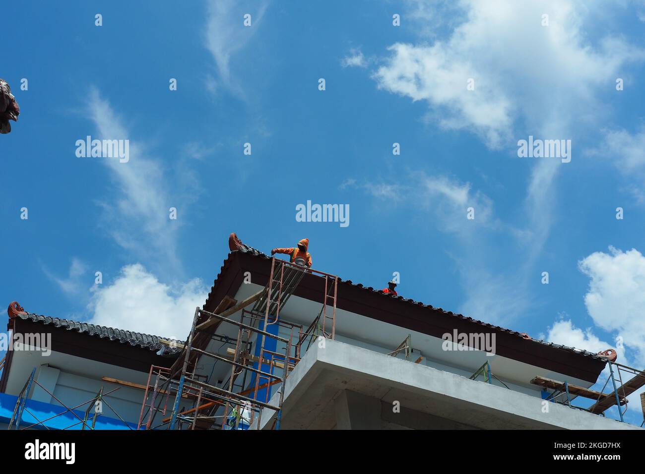 Bauarbeiter, die das Dach an Wolken befestigen, den blauen Himmel, Schindeln auf dem Dach des Hauses anbringen. Renovierung, Anstreichen der Wände, Verbesserung, Bau h Stockfoto