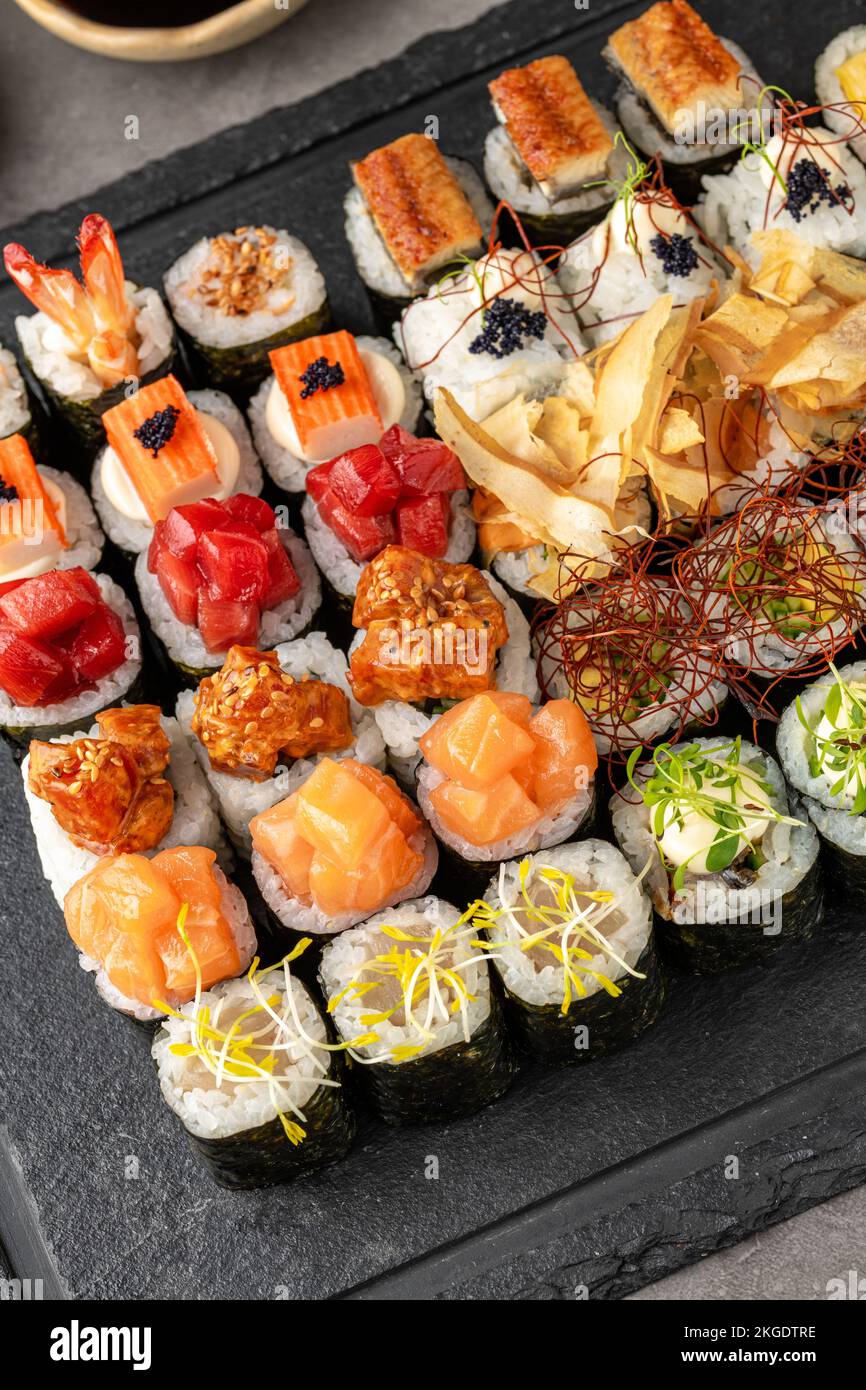 Sushi-Set mit verschiedenen Produkten auf einem schwarzen Steinteller. Verwischen Sie den Hintergrund und den selektiven Fokus Stockfoto