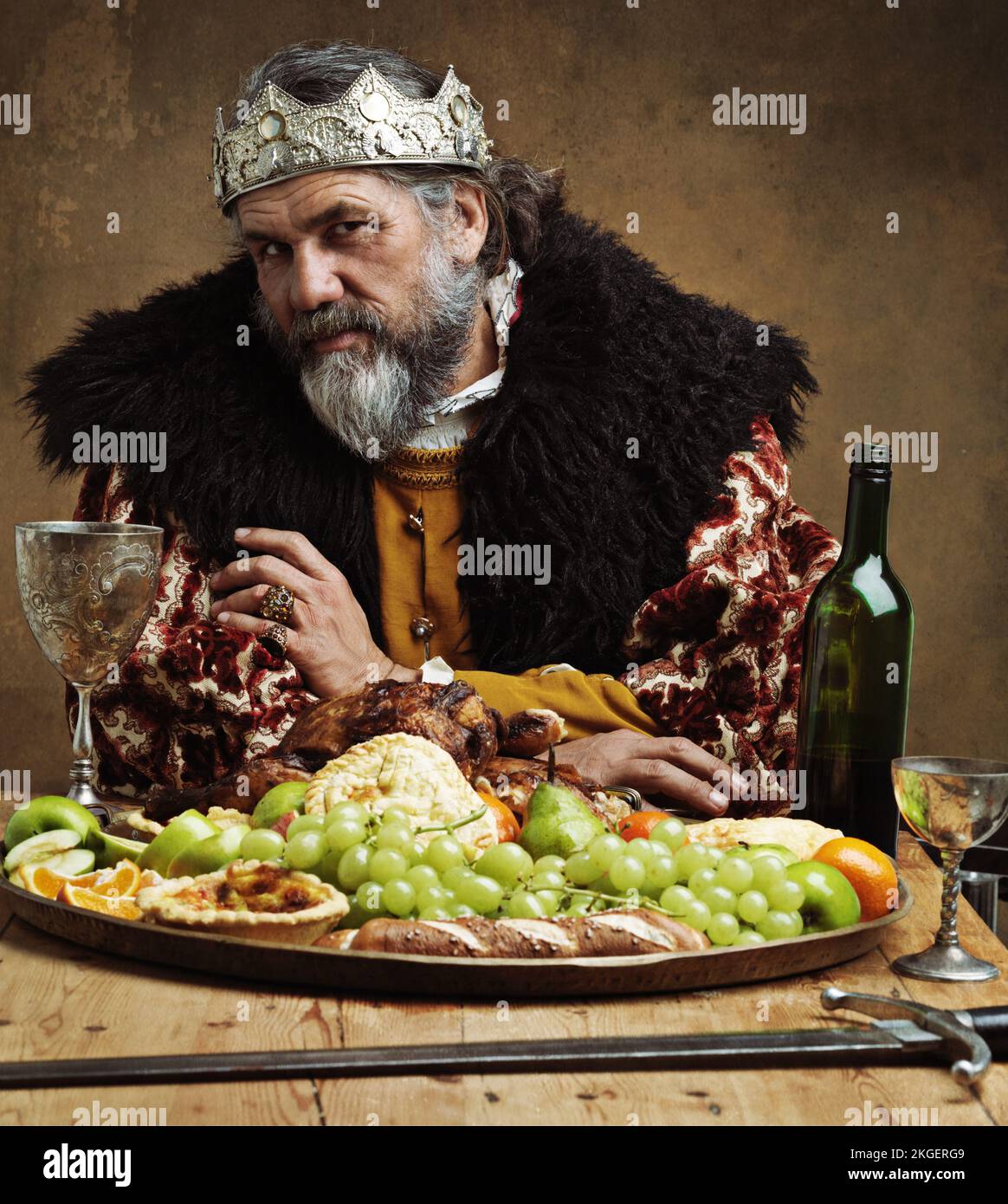 Oben ist es einsam. Ein reifer König, der allein in einem Bankettsaal feiert. Stockfoto