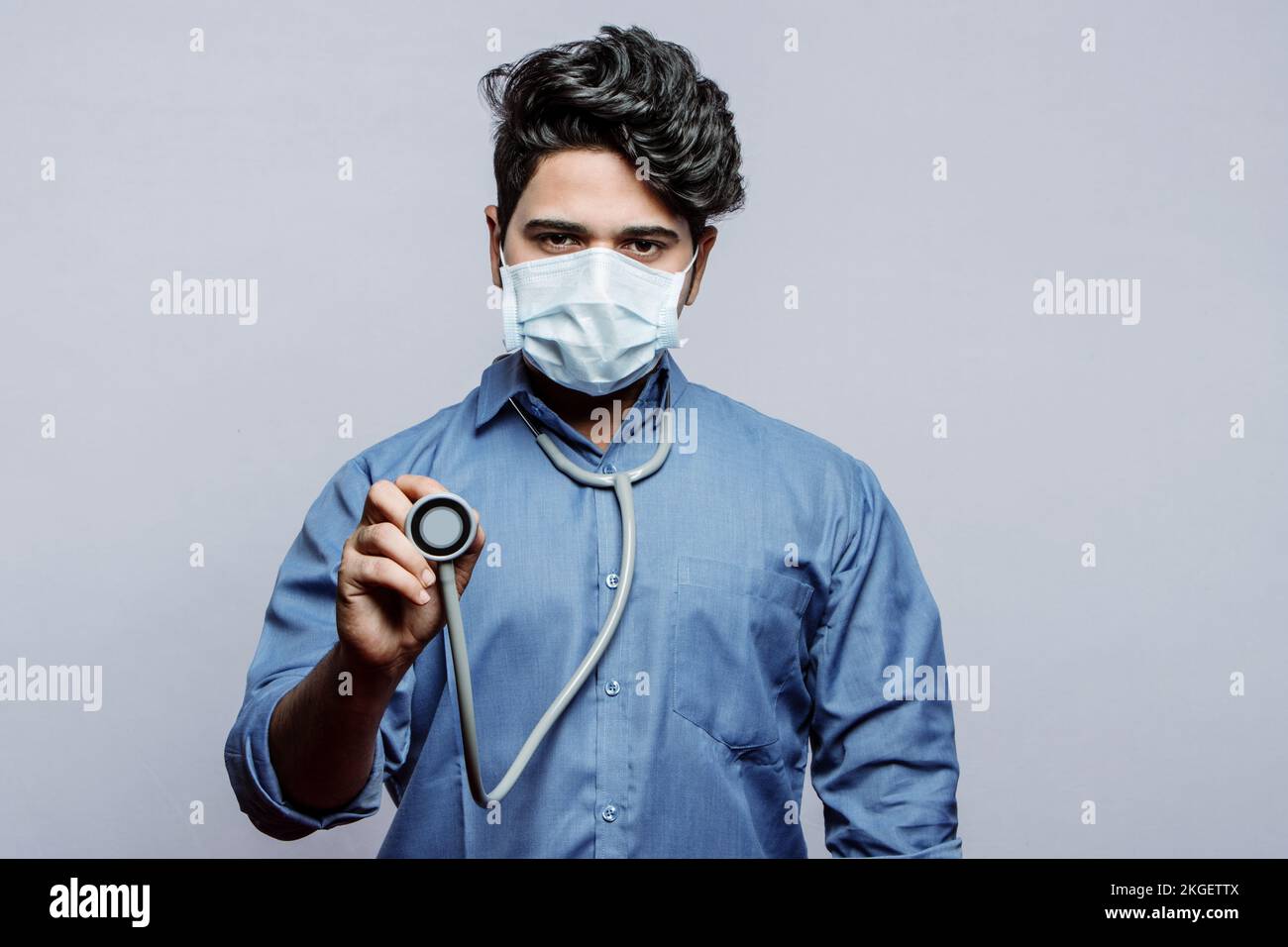 Lass mich nachsehen. Selektiver Fokus auf das Diaphragma eines Stethoskops in der Hand eines männlichen Arztes, der eine Maske auf grauem Hintergrund trägt. Stockfoto