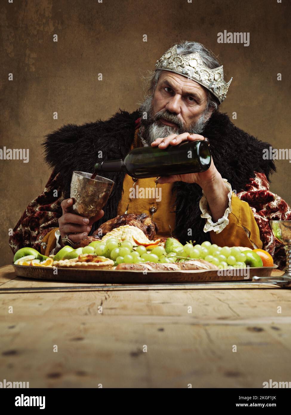 Ich glaube, ich brauche mehr Wein. Ein reifer König, der allein in einem Bankettsaal feiert. Stockfoto