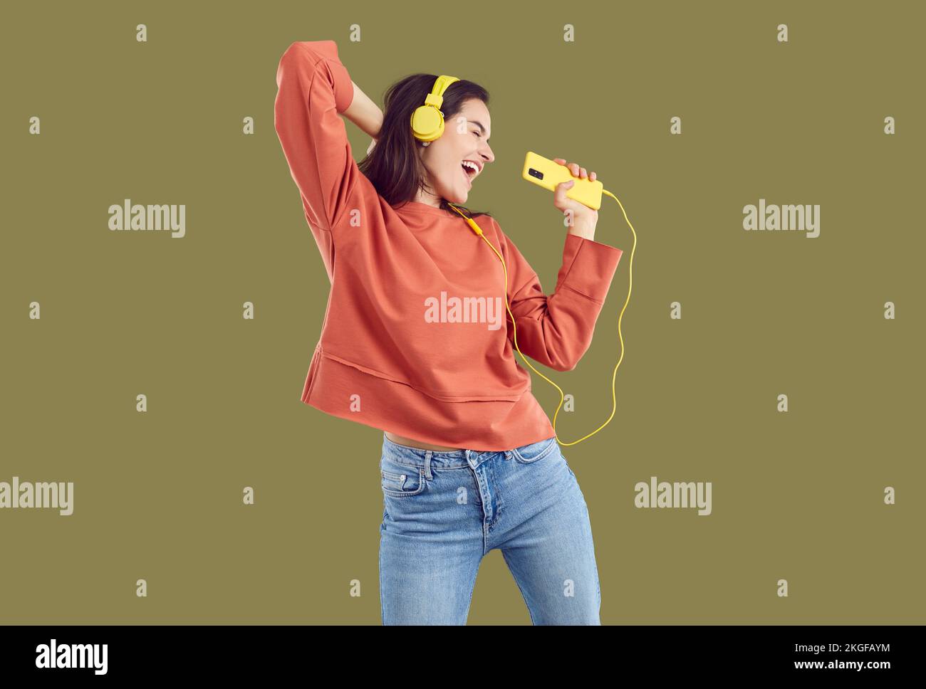 Brünette Frau in rotem Sweatshirt und Jeand, die Musik mit gelbem Smartphone und Headset hört. Stockfoto