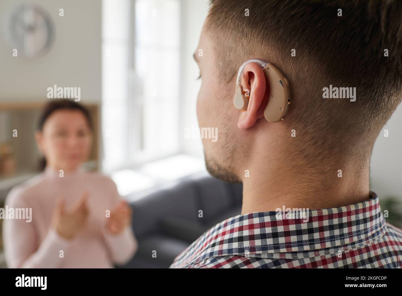 Tauber junger Mann, der ein Hörgerät am Ohr trägt und mit anderen Menschen kommuniziert Stockfoto