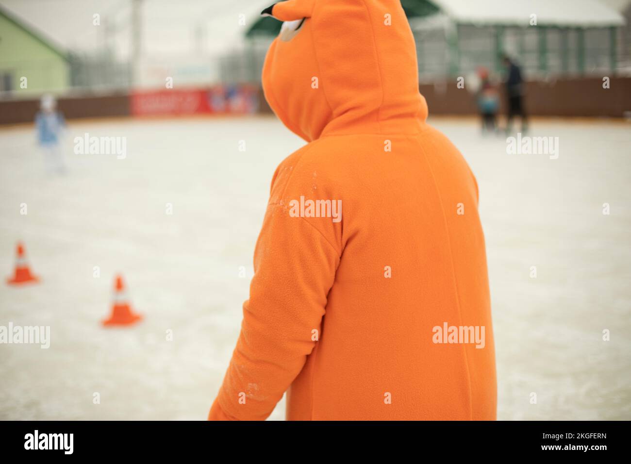 Orangefarbene Kleidung. Animator im Stadion im Winter. Schlittschuhlaufen. Details der Vorstellung auf Eis am Nachmittag. Stockfoto