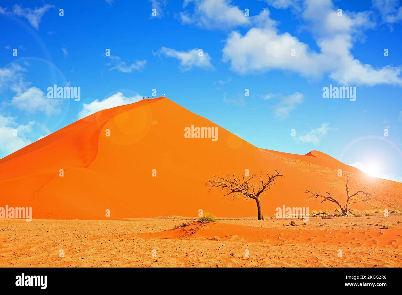 Weiter Blick auf die Menschen auf dem Gipfel einer hellen orangefarbenen Sanddüne mit einem hellblauen, wolkigen Himmel und Linsenerscheinungen in Namib-Wüste Namibia Stockfoto