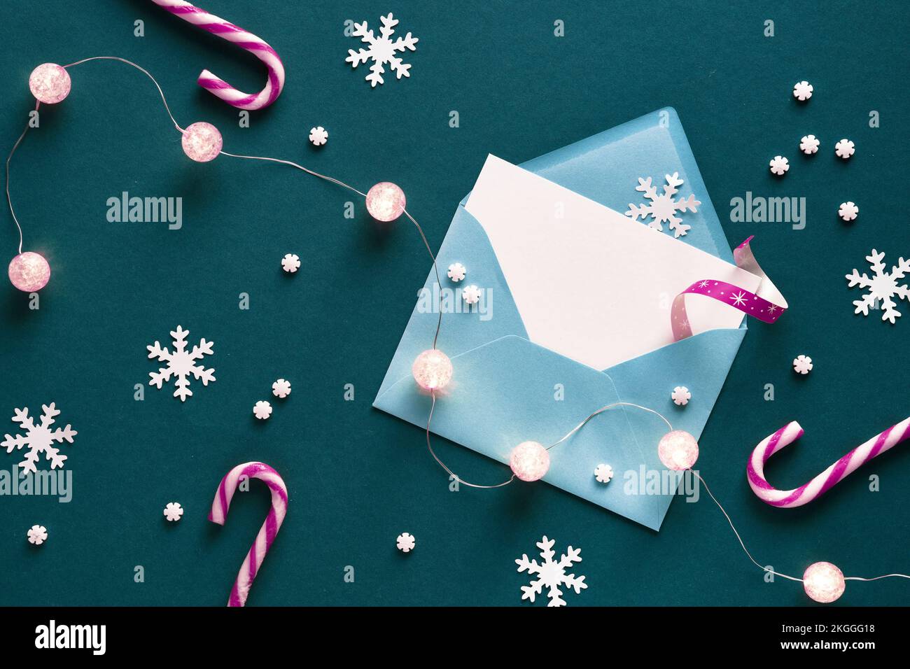 Grußkarte im Papierumschlag. Weihnachtshintergrund auf grünem Papier mit gestreifem Weiß, magentafarbenen Bonbons, Lichter Girlande, Schneeflocken. Draufsicht Stockfoto