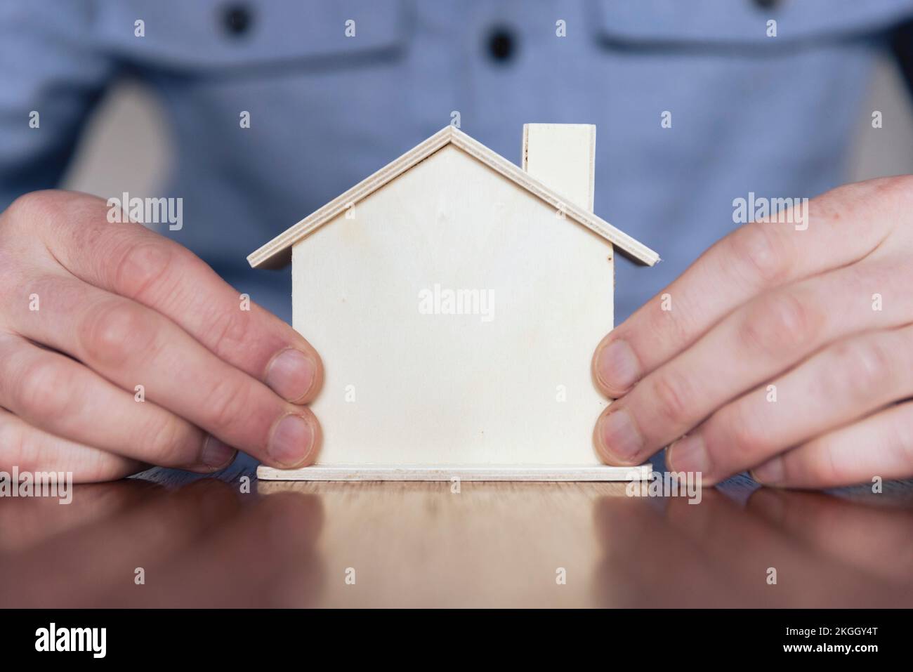 Hale Hände halten ein kleines Holzhaus. Immobilienmarktkonzept Stockfoto