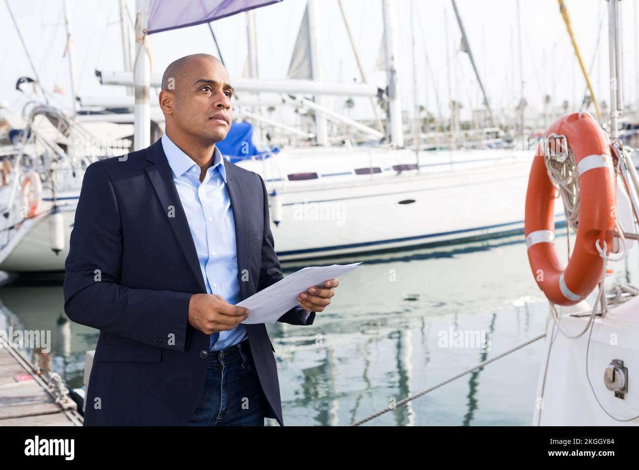 Lateinamerikanischer Mann mit Dokumenten in den Händen in der Nähe der Yacht im Seehafen Stockfoto