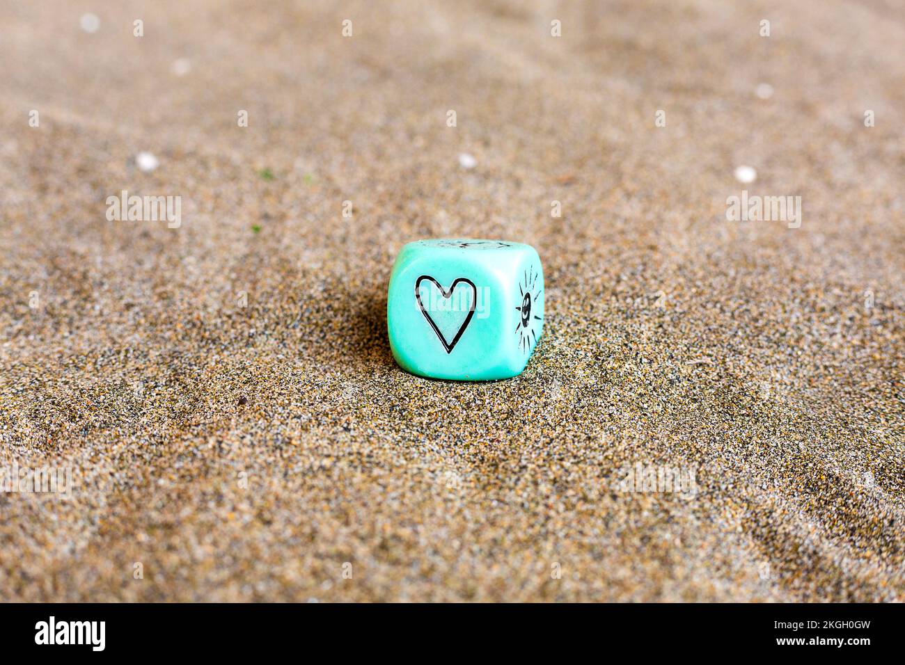 Herz- und Sonnenwettersymbole an den Seiten des blu-Plastikwürfels. Lustige Spielwürfel auf Sand. Valentinstag-Konzept. Liebessymbol. Nahaufnahme mit Stockfoto