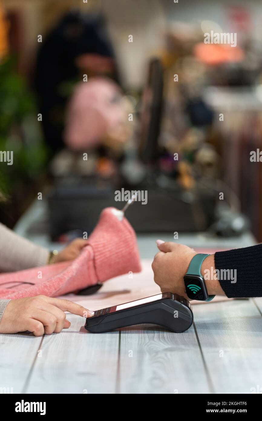 Ein Kunde, der mit einer Smart Watch in einem Bekleidungsgeschäft bezahlt, muss sich gegen eine Theke einlassen Stockfoto