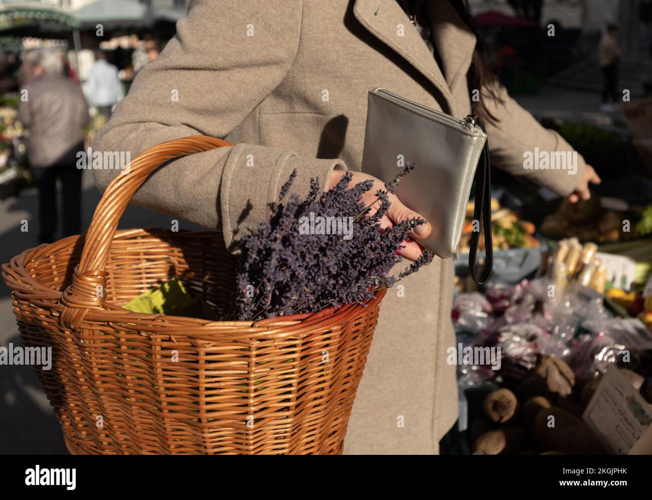 Eine Frau hält eine Handtasche und einen Korb Lavendel in der Hand und zeigt auf das Produkt, das sie kaufen möchte Stockfoto