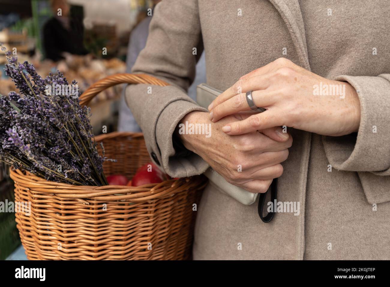 Eine Frau kam zum Einkaufen zum Supermarkt und hielt eine Handtasche und einen Korb mit Lavendel und Äpfeln in der Hand Stockfoto