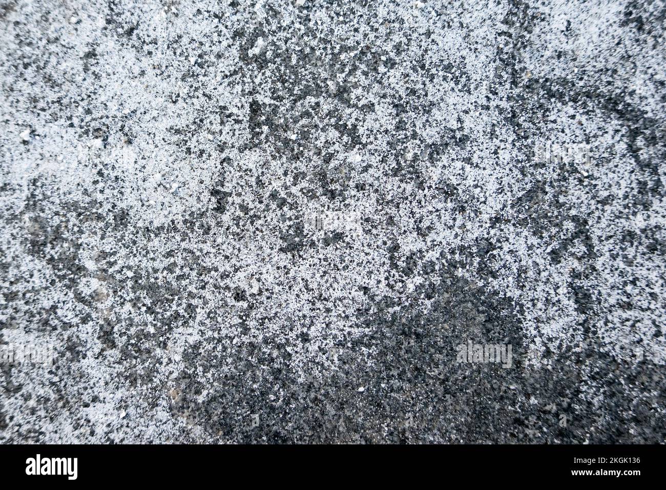 Salz verteilt auf eisigen Pflaster in der Stadt. Ziegel mit Salzflecken bedeckt. Rutschiger Gehweg im Winter. Stockfoto