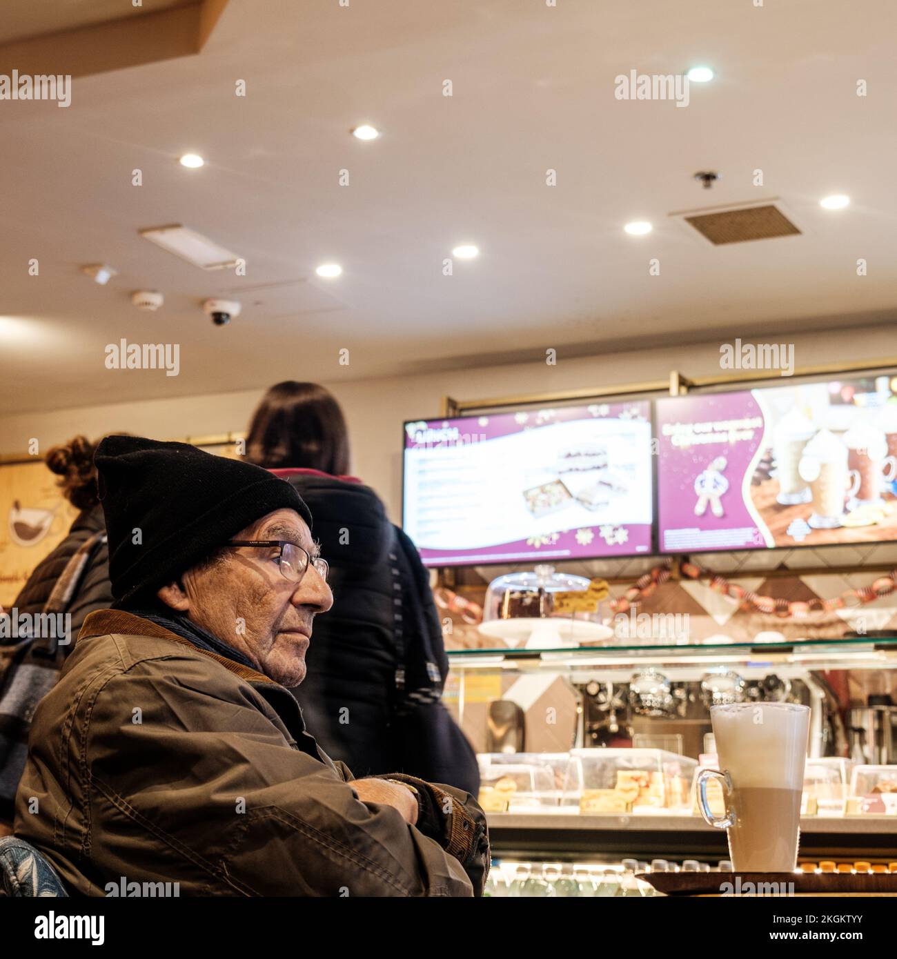 Epsom, Surrey, London, Großbritannien, November 20 2022, Seniorenmann mit Einem Latte-Kaffee, der während der Heizkostenkrise in Großbritannien warm bleibt und einen Woolen-Hut trägt Stockfoto