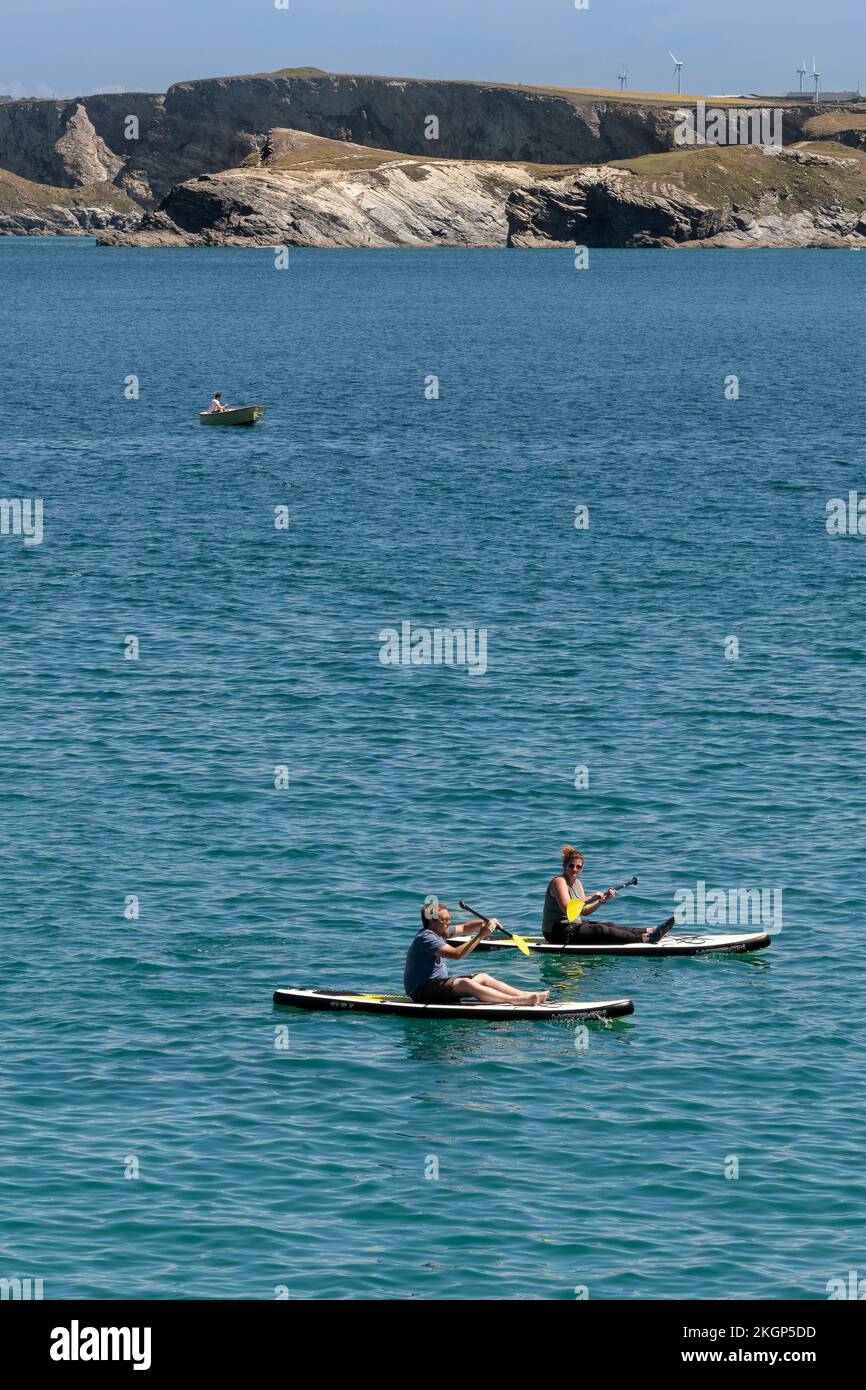 Zwei Urlauber sitzen auf Stand Up Paddleboards in Newquay Bay in Cornwall in England im Vereinigten Königreich. Stockfoto