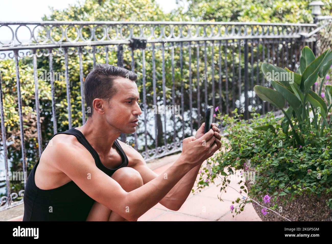 Mann fotografiert Pflanzen mit Smartphone in Pause auf dem Balkon Stockfoto