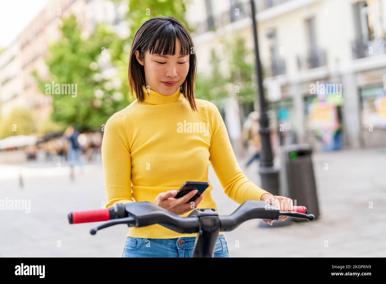 Junge Frau, die ein elektrisches Fahrrad über ein Smartphone freigibt Stockfoto