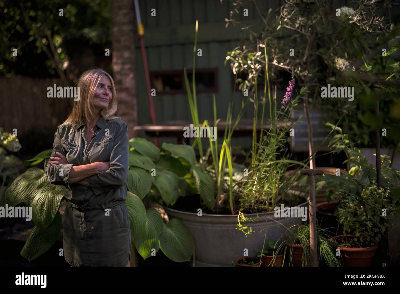 Lächelnde Frau, die mit gekreuzten Armen im Garten steht Stockfoto