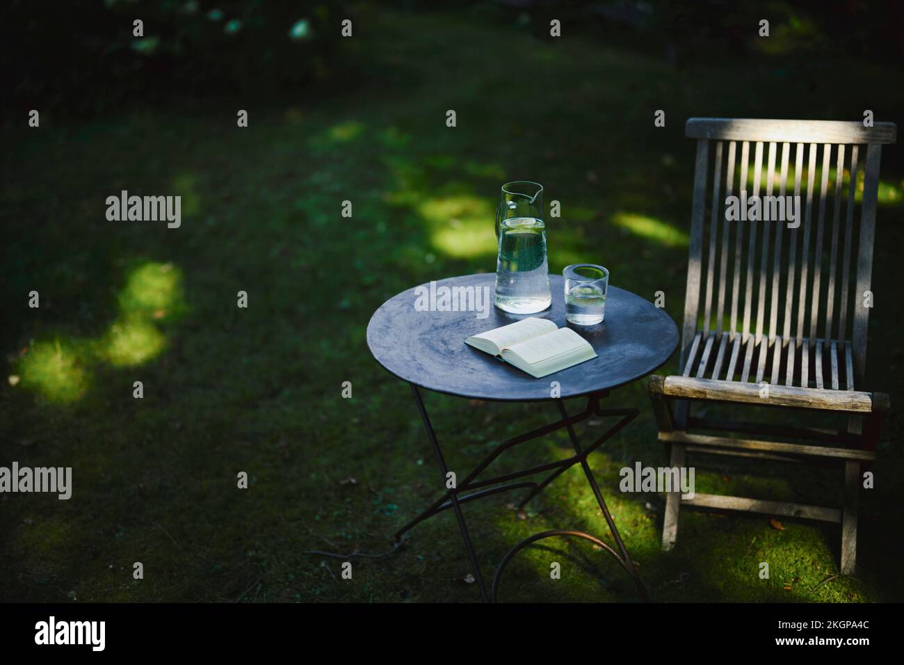 Offenes Buch und ein Glas Wasser auf dem Tisch mit Stuhl im Garten Stockfoto
