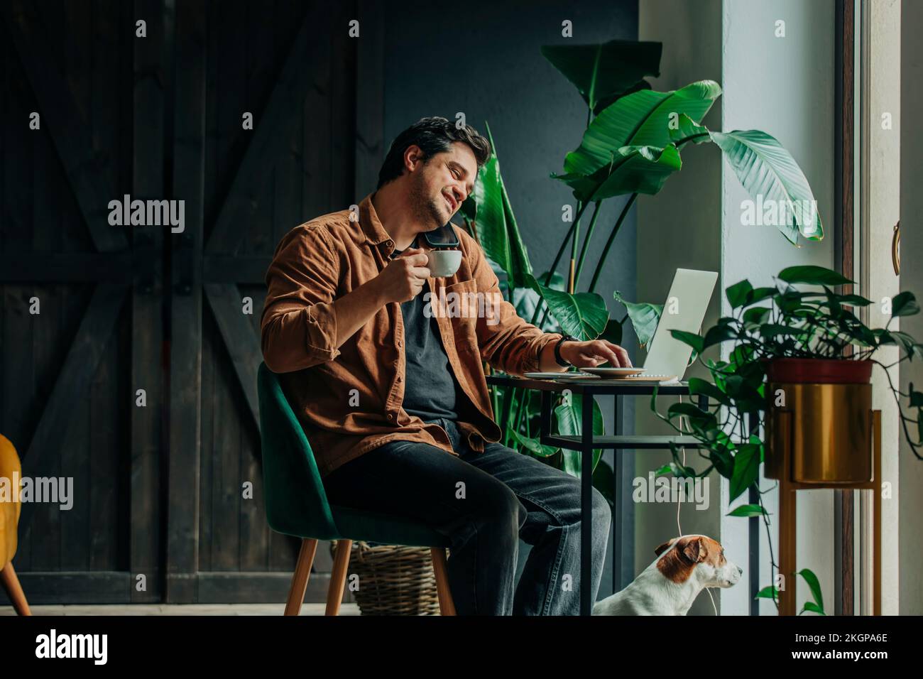 Freiberufler, der auf einem Smartphone spricht und die Tasse hält, sitzt im Heimbüro am Schreibtisch Stockfoto