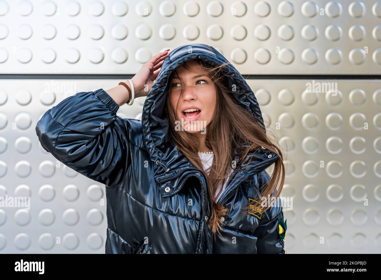 Eine Frau trägt eine schwarze, gepolsterte Jacke vor einer Metallwand Stockfoto