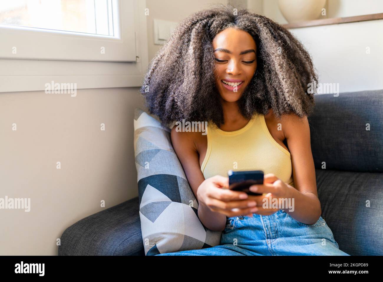 Eine Frau mit Afro-Haarschnitt, die zu Hause ein Handy benutzt Stockfoto