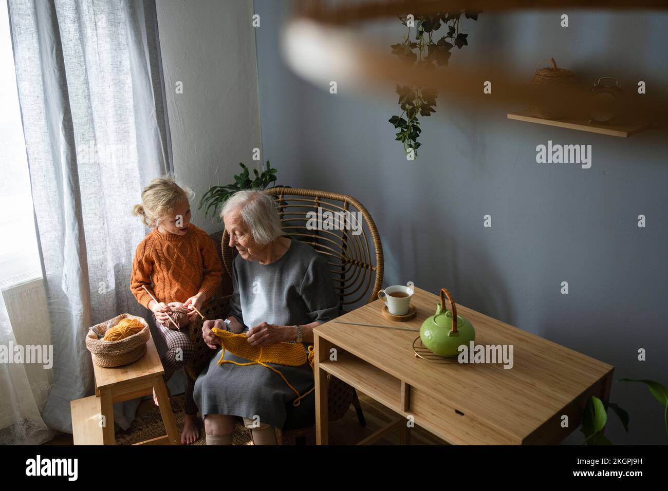 Großmutter schaut auf ein Mädchen, das Wollbälle im Wohnzimmer hält Stockfoto