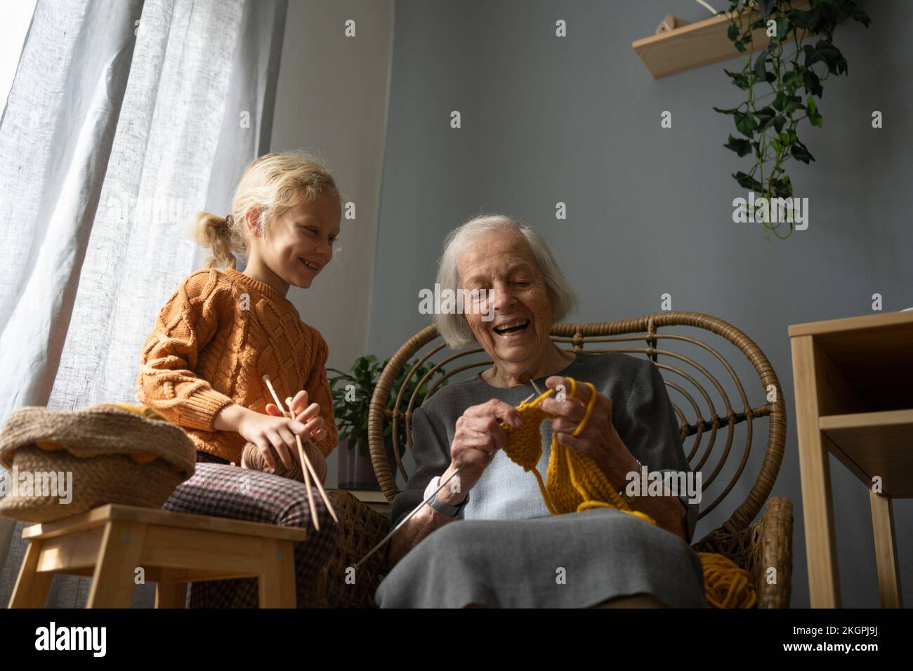 Glückliches Mädchen, das Wollknäuel und Nadel hält und Großmutter auf dem Stuhl strickt Stockfoto