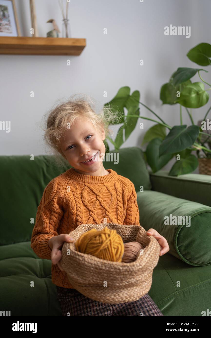 Lächelndes Mädchen, das zu Hause einen Wollball in einem Korb auf dem Sofa hält Stockfoto