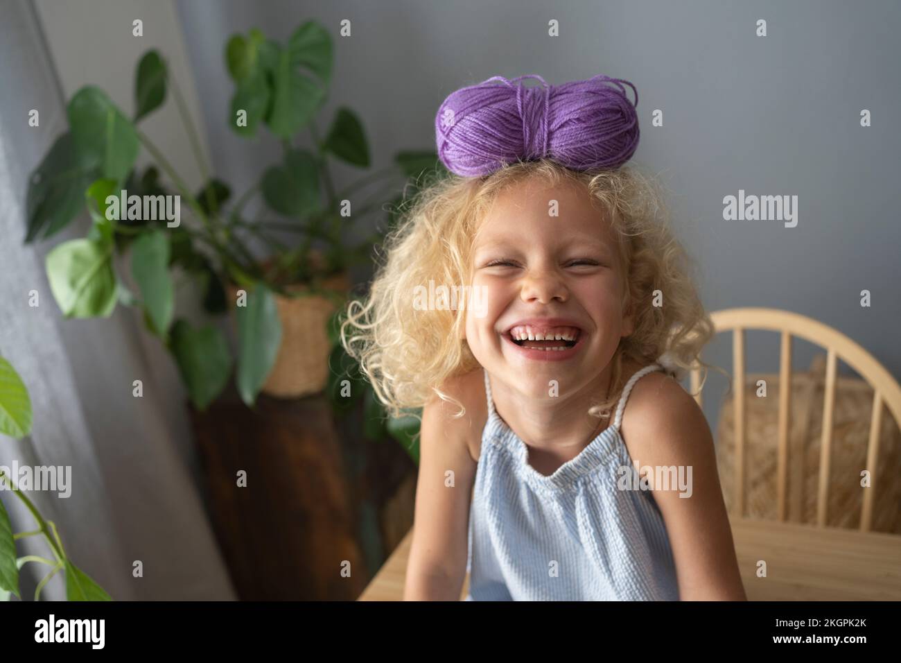 Glückliches Mädchen, das zu Hause Wollknäuel auf dem Kopf balanciert Stockfoto