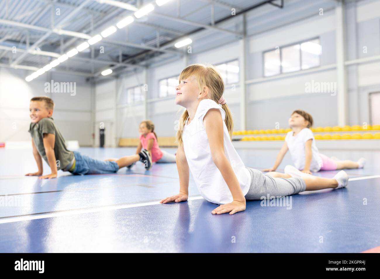 Lächelndes Schulmädchen, das sich mit Freunden auf dem Sportplatz streckt Stockfoto