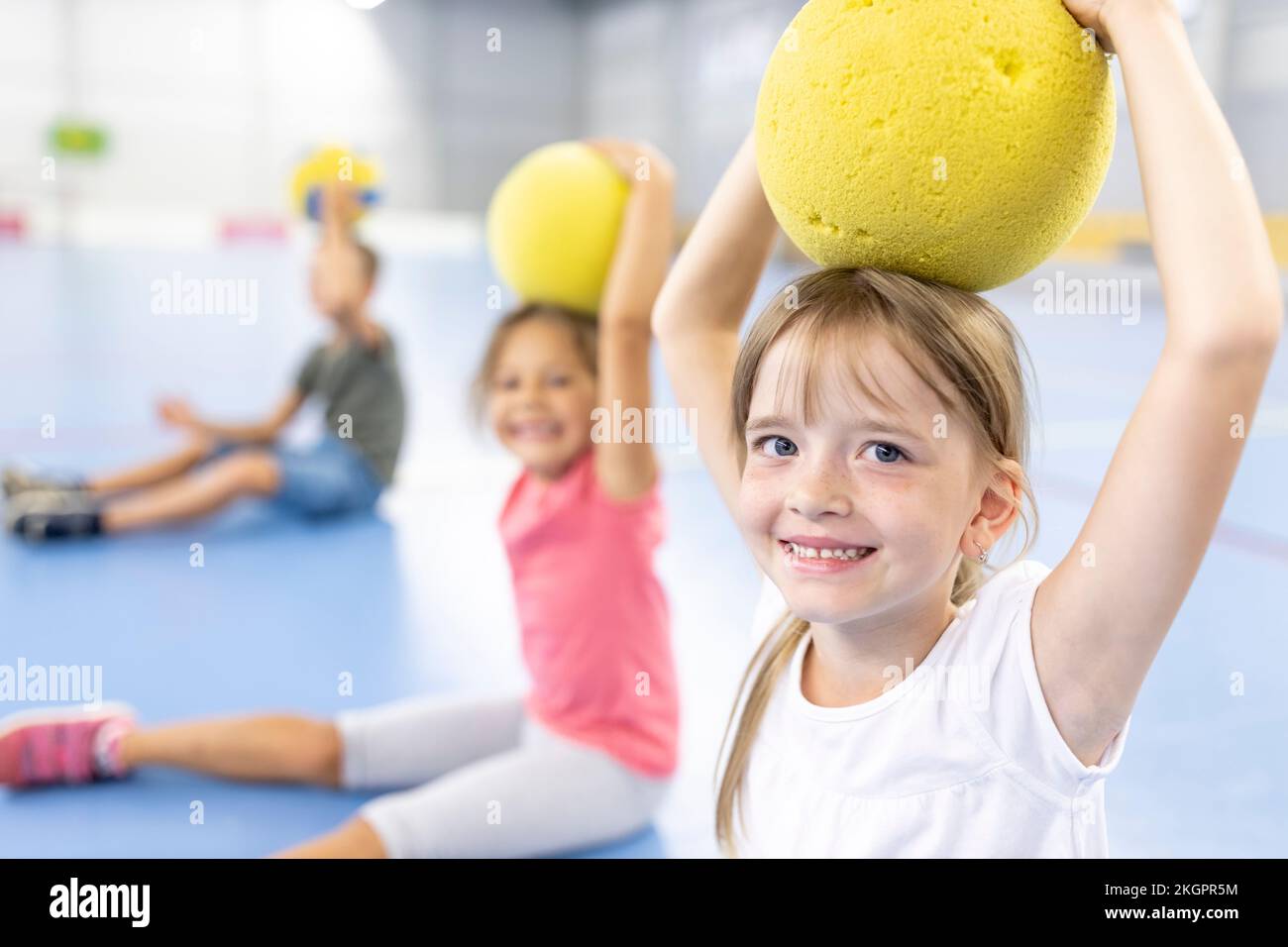 Lächelndes Mädchen, das auf dem Schulsportplatz Ball auf den Kopf hält Stockfoto