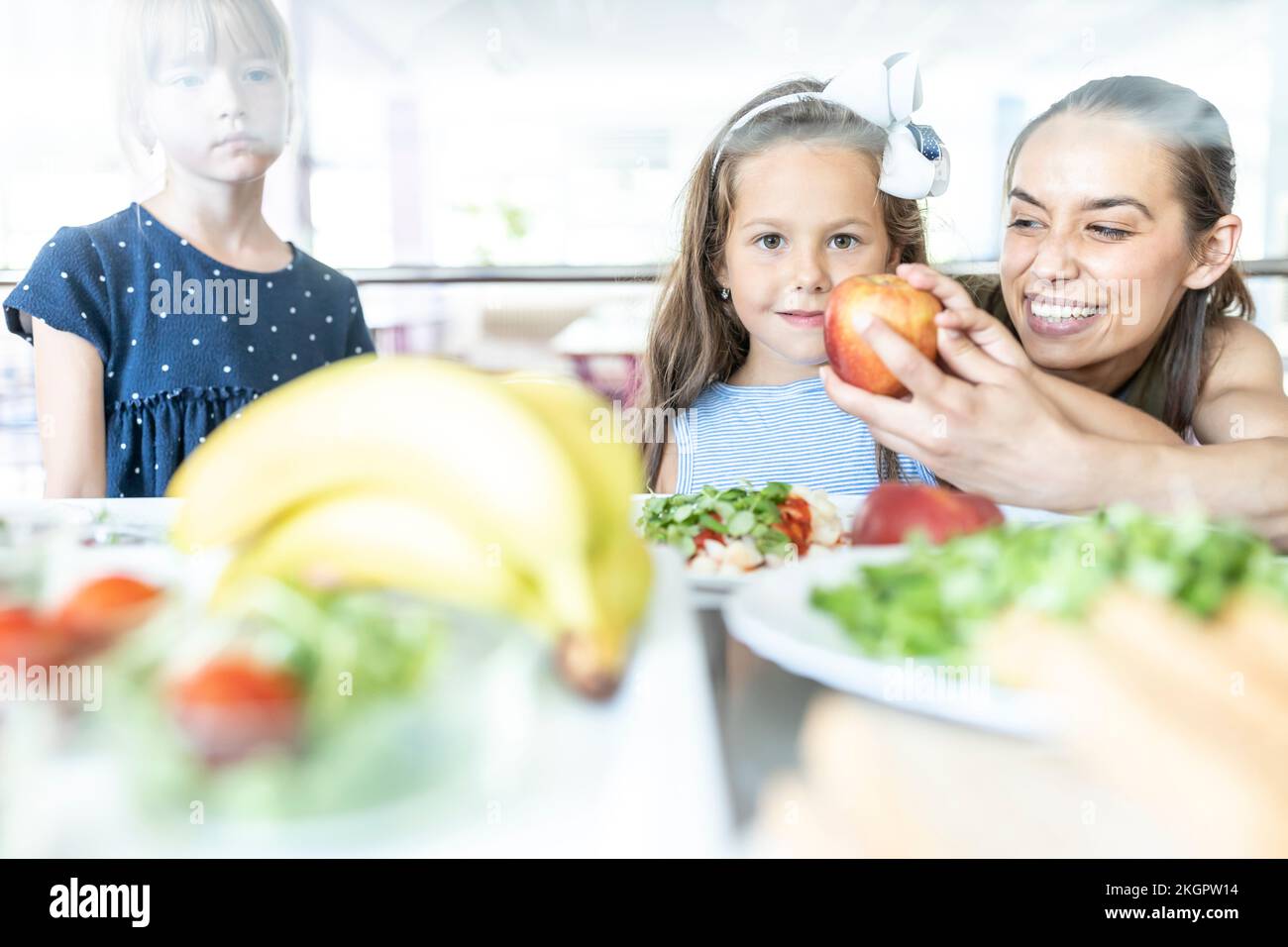 Lehrer gibt dem Schüler in der Schulkantine einen Apfel Stockfoto