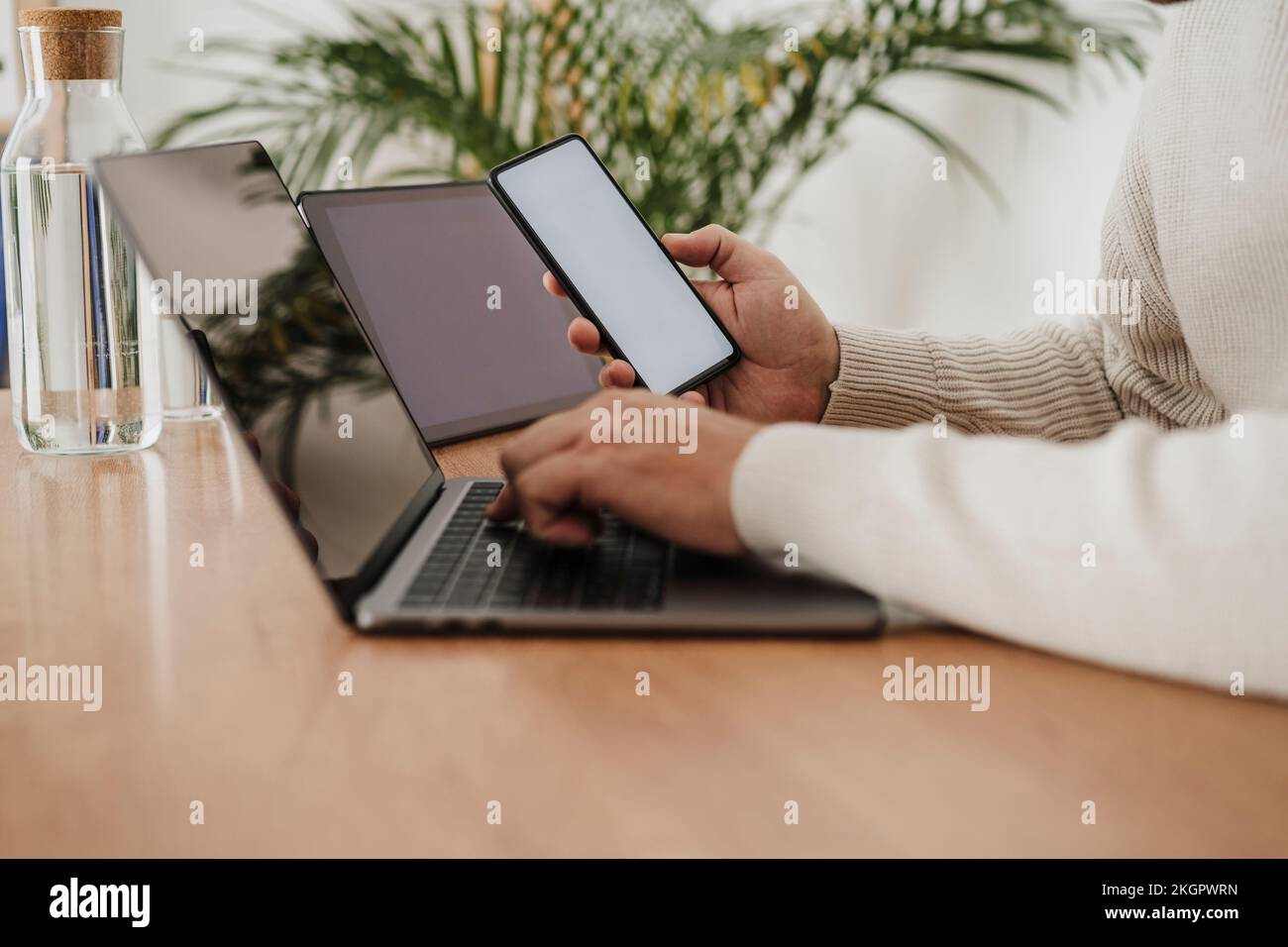 Hände eines Geschäftsmanns, der Laptop und Smartphone mit leeren Bildschirmen im Büro verwendet Stockfoto