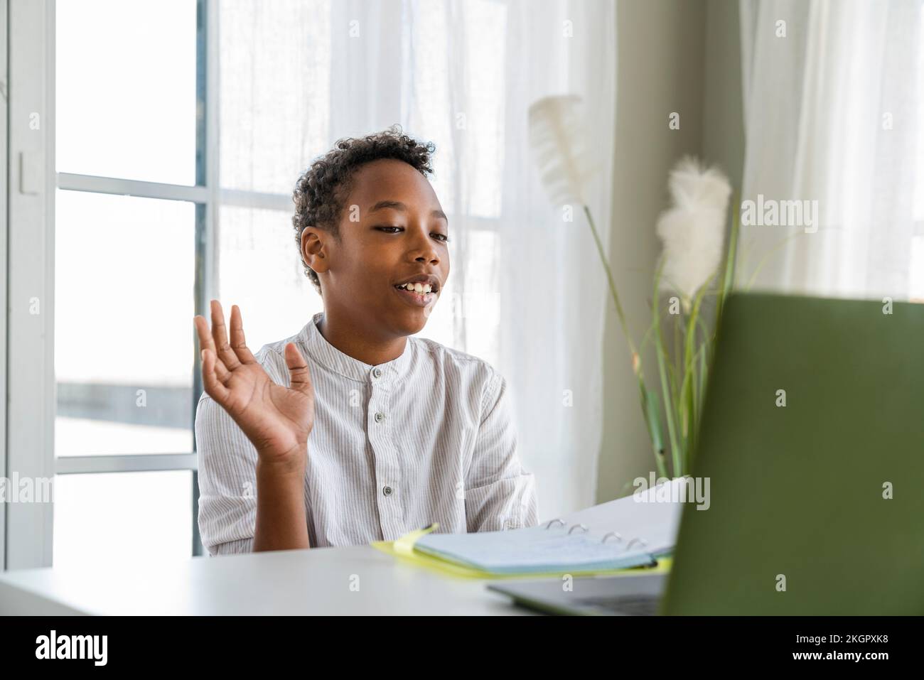 Ein Junge, der zu Hause bei einem Videoanruf über einen Laptop winkt Stockfoto