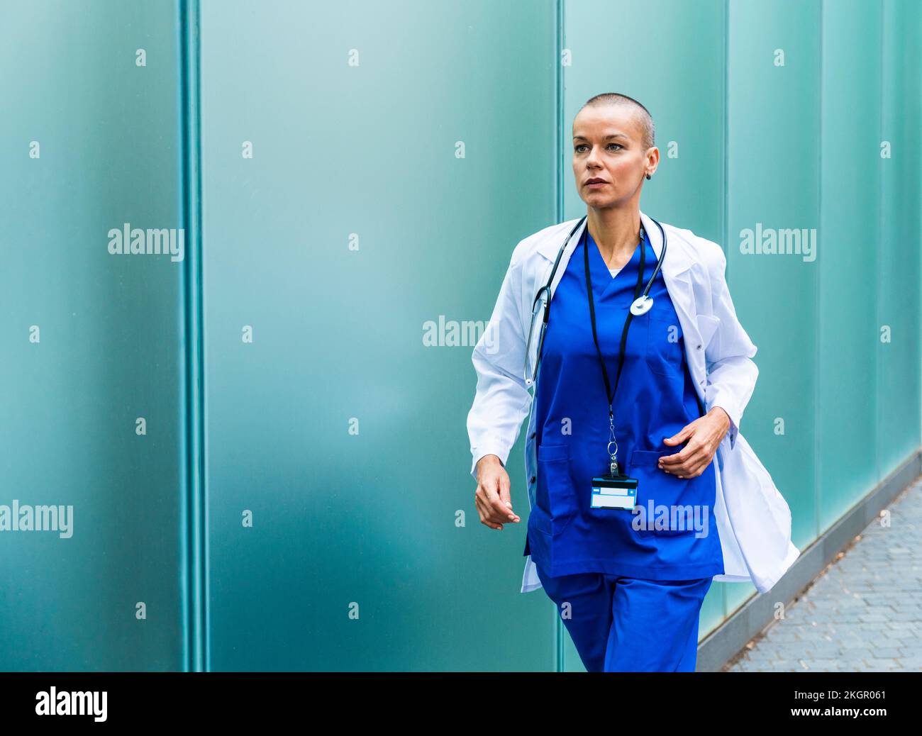 Reifer Arzt im Laborkittel, der an der Wand auf dem Fußweg läuft Stockfoto